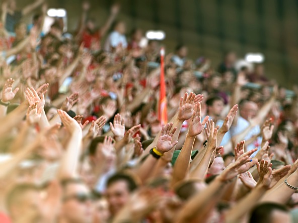 crowd of sports fans in a stadium, raising their hands